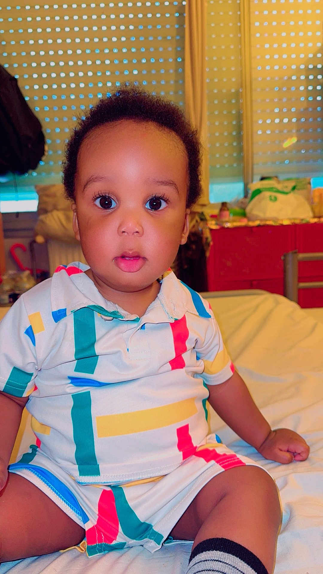 Raphaël participe au concours pour gagner de l'argent avec cette photo : child, toddler, baby, bed, clothing, striped, colorful, indoor, portrait, curious, face, person, sitting, window, blinds, furniture, sock, room, young_child, casual