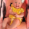 Ailany is registered to the contest to win money with this photo: baby, infant, smiling, yellow_clothing, headband, flower_headband, stroller, pink_stroller, sitting, happy, child, cute, hands_clasped, legs_crossed, indoors, plush, soft_texture, portrait, person, young_child