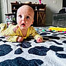 Bryce is registered to the contest to win money with this photo: baby, infant, yellow_pajamas, carpet, black_and_white_pattern, living_room, furniture, couch, cabinet, toys, curious_expression, floor, person, child, indoor, head, face, hands, bright_eyes, lying_down