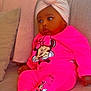 baby, child, infant, pink_clothing, turban, couch, blanket, pillow, socks, minnie_mouse, cartoon_character, indoor, seated, cute, soft_texture, cozy, portrait, casual, relaxed, looking_away