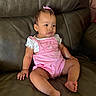 baby, child, pink_romper, bow, leather_couch, sitting, curious_expression, indoor, skin, foot, hand, earrings, short_hair, casual_clothing, infant, portrait, young_child, comfortable, furniture, home