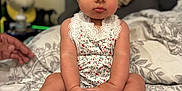 Olive is registered to the contest to win money with this photo: baby, bed, bedspread, child, cute, expression, fabric, feet, fingers, floral_outfit, flower_headband, hand, headwear, indoors, infant, person, portrait, room, sitting, skin