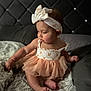 Olive is registered to the contest to win money with this photo: baby, child, tutu, headband, bow, bed, bedding, floral_pattern, sheet, curly_hair, infant, cute, chubby_cheeks, natural_light, soft_tones, sitting, indoors, portrait, clothing, foot