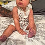 Olive is registered to the contest to win money with this photo: arm, baby, bed, bedspread, cap, child, cute, face, flower, headband, headboard, indoors, infant, looking_up, pattern, person, romper, sitting, skin, tattoo
