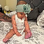 Olive is registered to the contest to win money with this photo: arm, baby, bed, bedspread, child, curious, cute, floral, flower, headband, indoors, infant, looking_down, person, portrait, sitting, skin, soft_lighting, tattoo, young_child