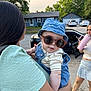 Matthew is registered to the contest to win money with this photo: baby, sunglasses, denim, bucket_hat, person, child, outdoor, street, car, house, holding, clothing, summer, casual, plaid_skirt, tumbler, drink, shoes, green_shirt, portrait