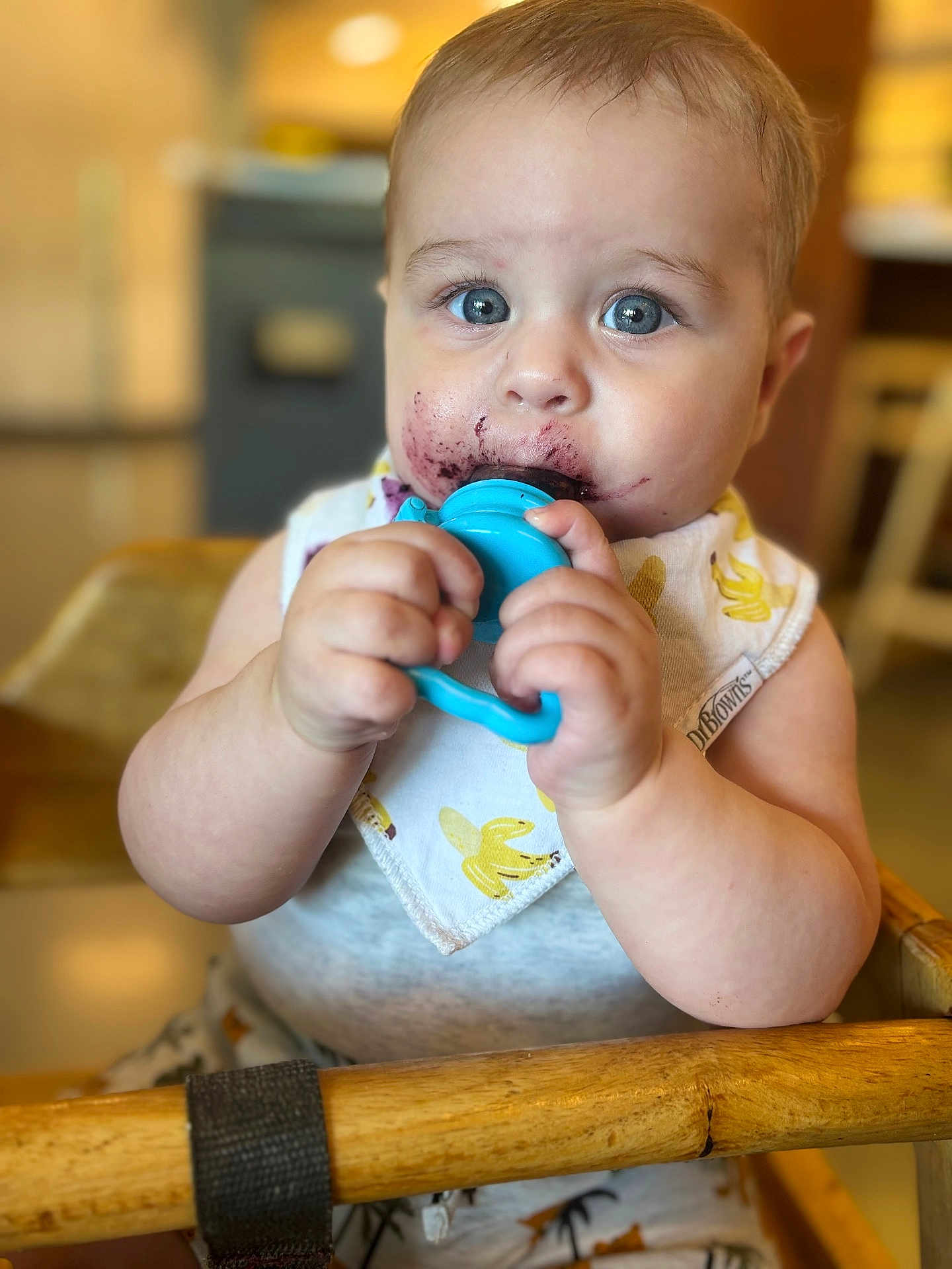 Matthew is registered to the contest to win money with this photo: baby, blue_eyes, bib, bananas, blue_teething_toy, chubby_cheeks, clothing, face, food_mess, high_chair, indoor, kitchen, person, plush, portrait, sitting, teething_toy, wood, young_child, cute