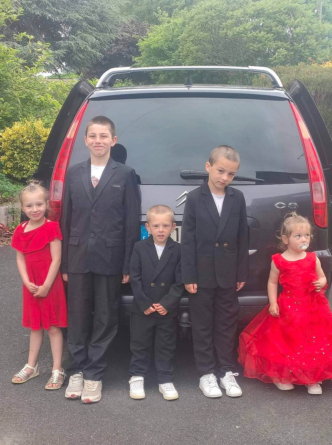 Mila participe au concours pour gagner de l'argent avec cette photo : automotive_exterior, blazer, car, coat, dress, event, face, formal_wear, gesture, joy, motor_vehicle, person, plant, smile, suit, tie, tire, tree, vehicle, vehicle_door