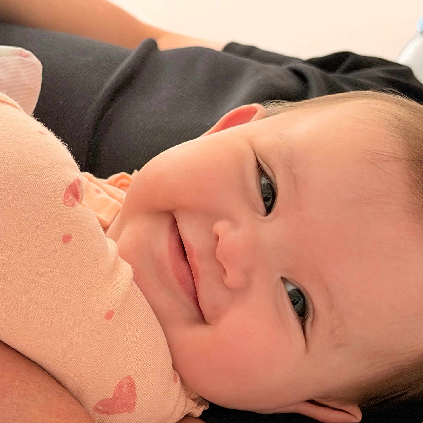 Megan joined the competition — help win amazing prizes! baby, smile, face, infant, skin, person, arm, clothing, fabric, pattern, heart, resting, closeup, happy, cute, young_child, indoor, soft_light, bottle, background