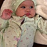 baby, infant, child, onesie, bonnet, floral_pattern, blanket, soft_fabric, couch, leather, cute, chubby_cheeks, portrait, indoors, relaxed, gazing, hand_raised, comfortable, cozy, young