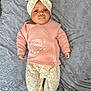 baby, infant, headband, pink_clothing, floral_pants, blanket, lying_down, indoors, cute, child, portrait, sleepwear, cozy, soft_texture, newborn, small_hands, footed_pants, expressionless, comfortable, bedspread