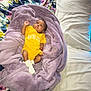 baby, infant, blanket, yellow_onesie, bed, pillow, floral_pattern, purple_blanket, lying_down, indoors, soft_texture, cute, child, person, sleepwear, resting, skin, face, head, footwear