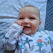 Maël participe au concours pour gagner de l'argent avec cette photo : baby, smiling, infant, onesie, patterned_clothing, hand, face, lying_down, blanket, cute, happy, child, playful, indoor, closeup, skin, head, eyes, mouth, cheeks