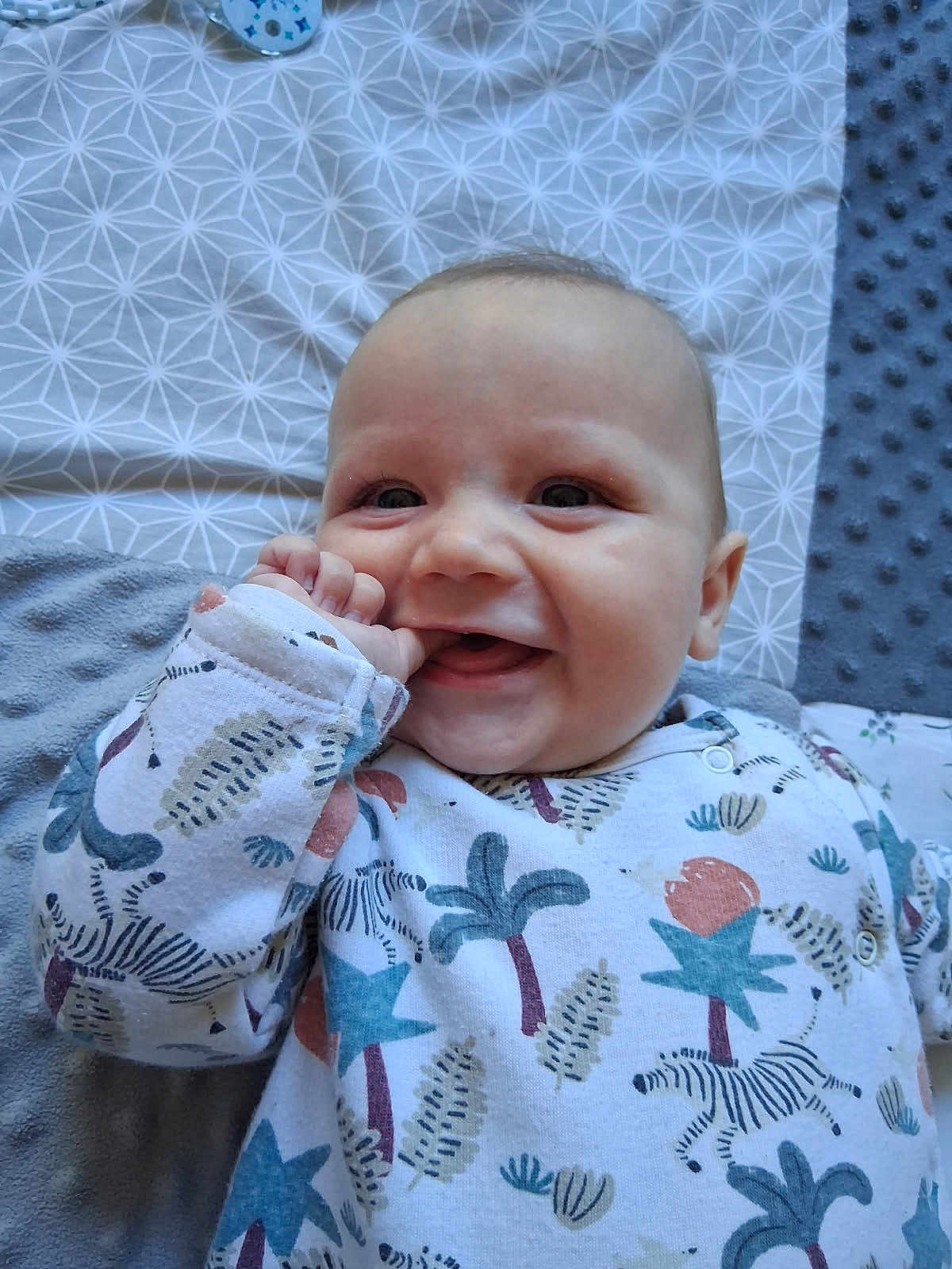 Maël participe au concours pour gagner de l'argent avec cette photo : baby, smiling, infant, onesie, patterned_clothing, hand, face, lying_down, blanket, cute, happy, child, playful, indoor, closeup, skin, head, eyes, mouth, cheeks