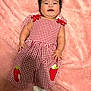 Victoria Evangeline is registered to the contest to win money with this photo: baby, blanket, checkered, child, clothing, cute, dress, happy, indoors, infant, lying_down, person, pink_background, portrait, red_and_white, small_hands, smiling, socks, soft_texture, strawberry_patch
