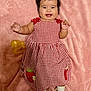 baby, checkered, child, cute, dress, face, happy, indoors, infant, lying_down, pink_blanket, playful, portrait, red_and_white, shoe, smiling, sock, strawberry_patch, toy, yellow_bow