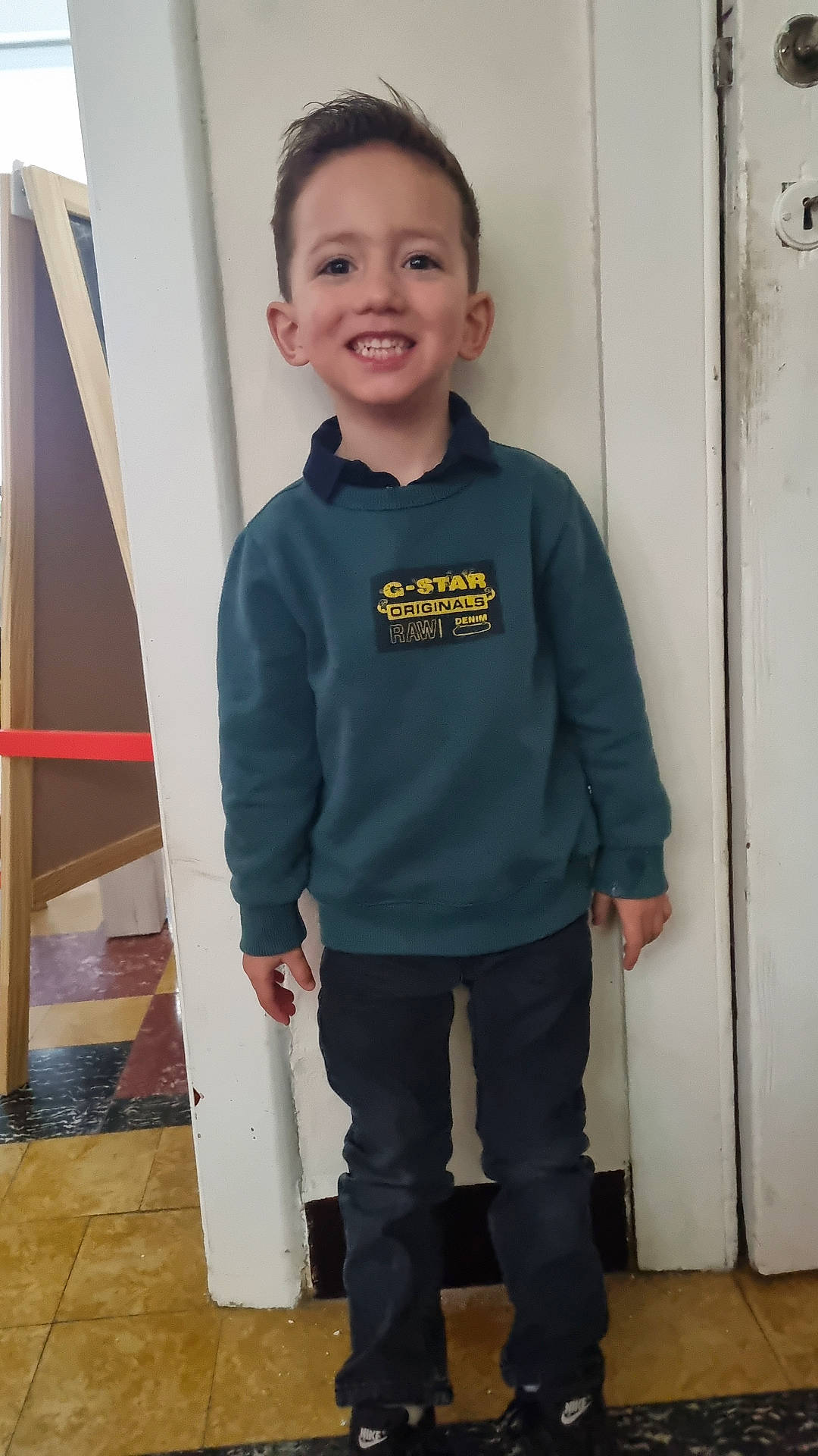 Angelo participe au concours pour gagner de l'argent avec cette photo : boy, casual, child, clothing, door, face, floor, footwear, hair, happy, indoor, pants, person, portrait, shoes, smile, standing, sweatshirt, wall, young