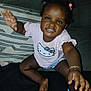 Shameria is registered to the contest to win money with this photo: toddler, child, smiling, hello_kitty, shirt, bracelet, couch, pillow, indoor, happy, person, sitting, hair_buns, barefoot, playful, portrait, young_child, dark_skin, cute, clothing