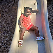Shameria is registered to the contest to win money with this photo: toddler, child, slide, playground, outdoor, sunlight, smiling, happy, shoes, shorts, hair_buns, summer, fun, play, active, recreation, casual, daytime, person, leisure