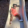 toddler, child, slide, playground, outdoor, sunlight, smiling, happy, shoes, shorts, hair_buns, summer, fun, play, active, recreation, casual, daytime, person, leisure