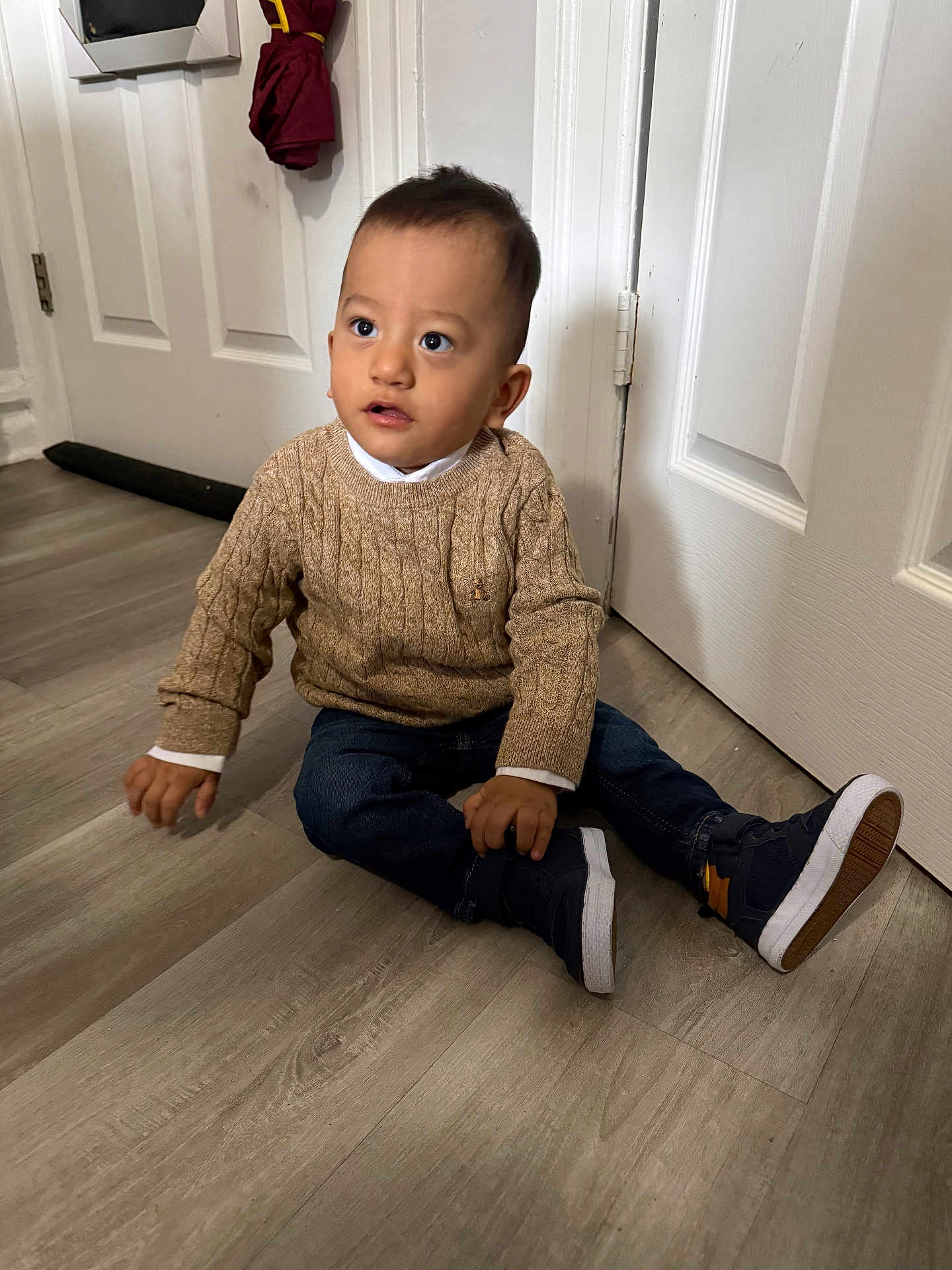 Theo joined the competition — help win amazing prizes! toddler, child, sitting, indoor, floor, door, sweater, jeans, shoes, umbrella, curious, young_child, casual_clothing, wooden_floor, white_door, portrait, person, cute, indoors, young_kid