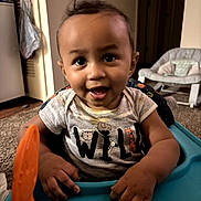 Alijah is registered to the contest to win money with this photo: toddler, child, smile, high_chair, toy, indoor, living_room, carpet, shirt, short_sleeve, person, face, hand, hair, happy, furniture, door, plastic, baby, seat