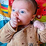 baby, infant, child, face, hand, thumb, clothing, brown_outfit, play_mat, colorful_background, cute, expression, portrait, indoors, young_child, soft_texture, animal_pattern, closeup, person, newborn