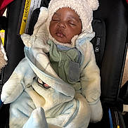 Romney Tau is registered to the contest to win money with this photo: baby, bundle, car_seat, child, clothing, coat, comfort, cute, face, hat, headwear, indoors, infant, portrait, rest, seat, sleeping, soft, warm, warning_label