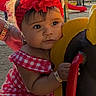 baby, child, toddler, playground, outdoor, portrait, flower_headband, red_dress, gingham, smiling, face, eyes, sitting, playground_ride, playground_equipment, hand, bracelet, park, trees, phone_screenshot