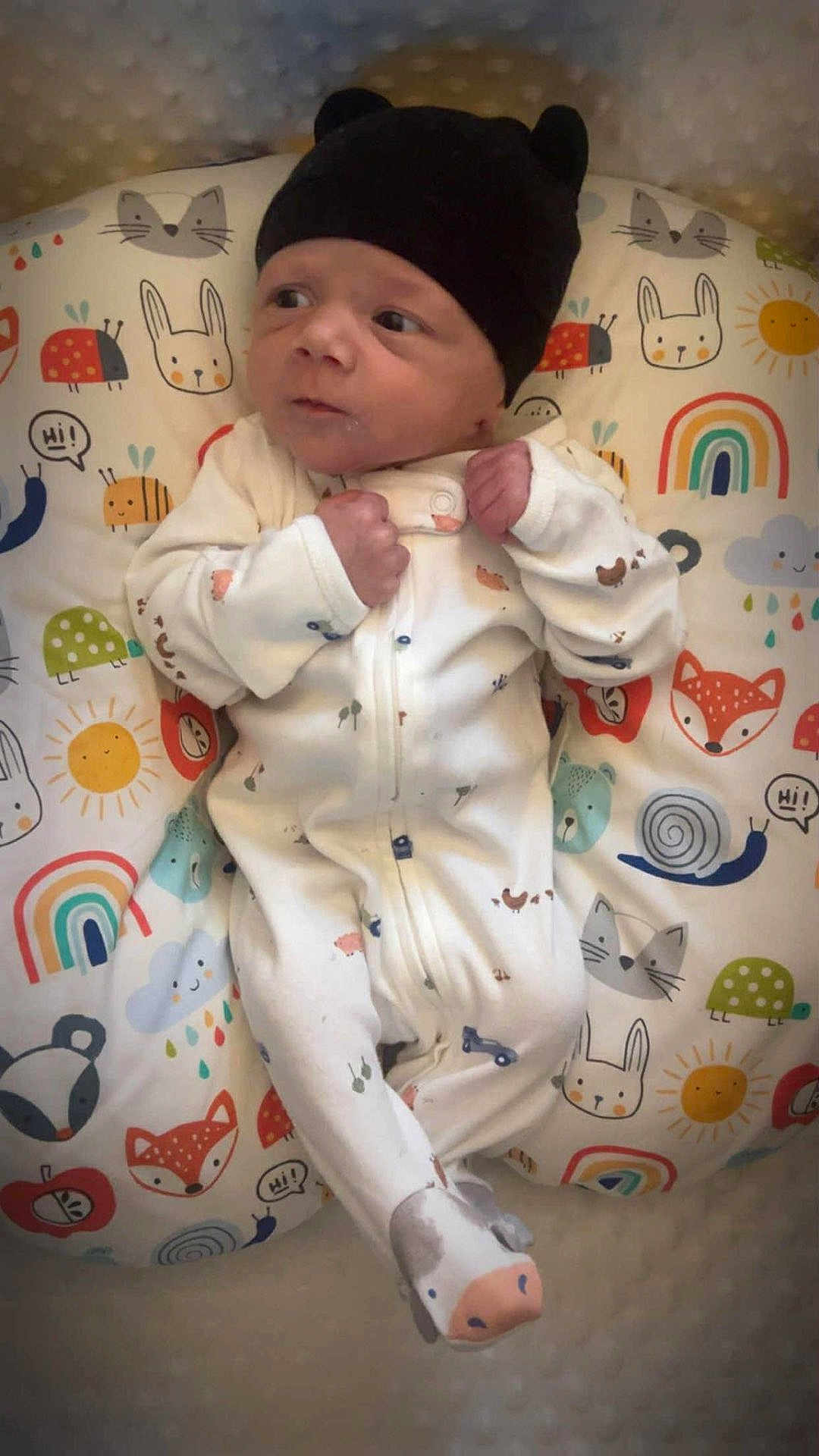 Jamison joined the competition — help win amazing prizes! baby, infant, newborn, onesie, hat, black_hat, animal_print, pillow, colorful, pattern, cute, clothing, lying_down, fist, face, headwear, child, indoors, soft_lighting, curious