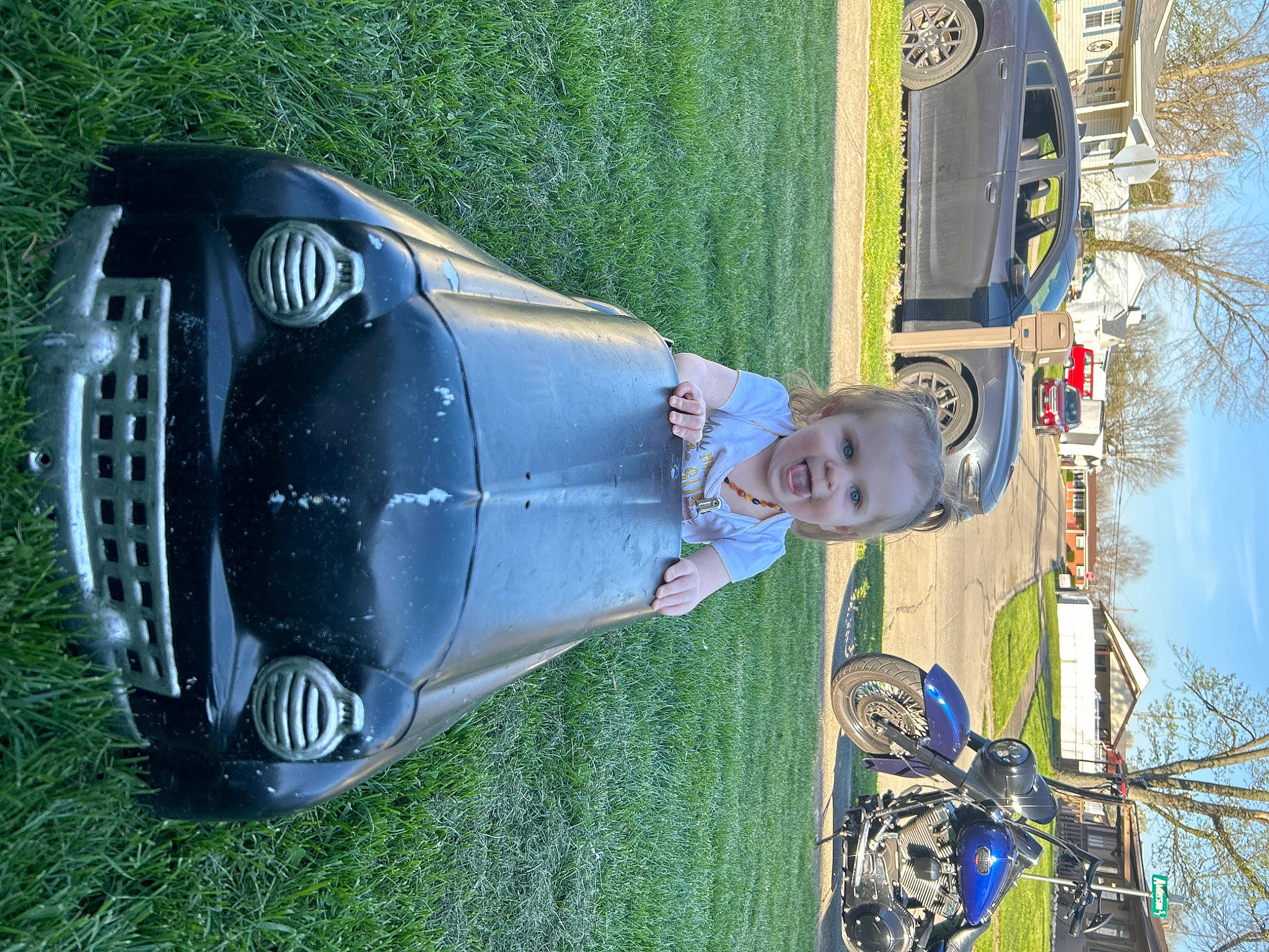 Charlotte is registered to the contest to win money with this photo: automotive_design, automotive_exterior, automotive_lighting, automotive_tire, bumper, car, electric_blue, fender, grass, hood, motor_vehicle, person, plant, sky, smile, tire, tree, vehicle, vehicle_door, wheel