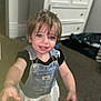 Mia joined the competition — help win amazing prizes! toddler, child, denim_overall, white_skirt, carpet, indoor, blue_eyes, blond_hair, furniture, dresser, person, smiling, cute, reaching_hand, young_child, clothing, room, home, portrait, playing