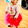 toddler, child, birthday, pink_tutu, white_shirt, number_one, standing, wooden_floor, indoor, curly_hair, celebration, cute, smiling, person, young_child, clothing, footwear, home, happy, party