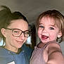 Mia is registered to the contest to win money with this photo: child, woman, glasses, smile, indoor, hoodie, name_tag, person, happy, face, blue_eyes, short_hair, casual_clothing, portrait, family, people, closeup, toddler, adult, holding