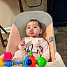baby, child, high_chair, toy, colorful, pajamas, indoor, floor_tile, plastic, face, expression, pucker, seat, play, infant, person, home, cute, furniture, activity
