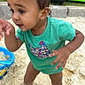 toddler, child, baby, portrait, outdoor, playground, sand, summer, turquoise_shirt, floral_shirt_design, curly_hair, brown_eyes, smiling, curious, standing, barefoot, adult_hand, playground_toy, backyard, daylight