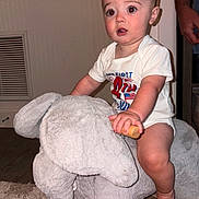 Grayson joined the competition — help win amazing prizes! baby, child, indoor, plush_toy, rocking_elephant, carpet, hand, tattoo, wooden_handle, shirt, expression, face, foot, furniture, person, room, wall, floor, toy, candid