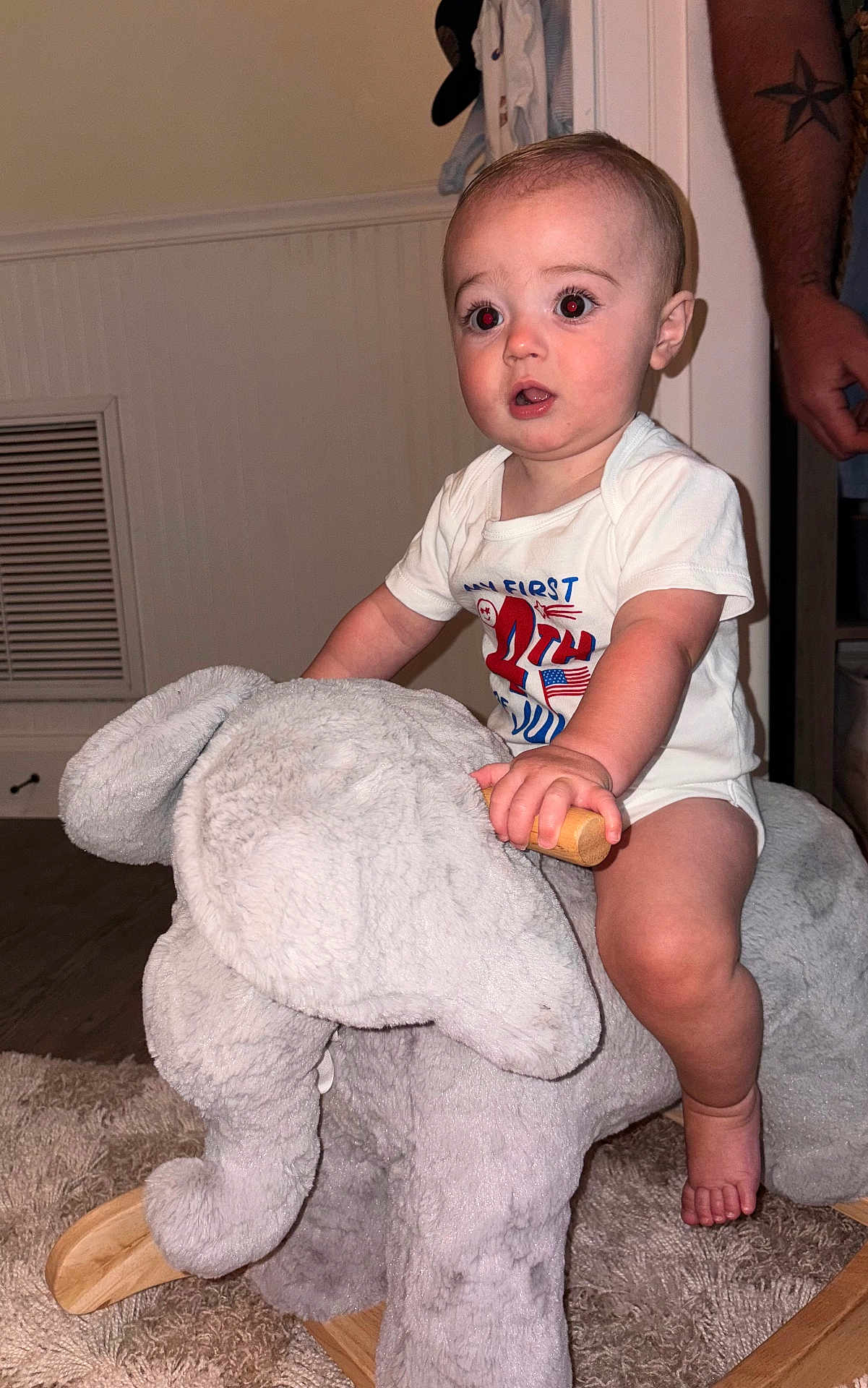 Grayson joined the competition — help win amazing prizes! baby, child, indoor, plush_toy, rocking_elephant, carpet, hand, tattoo, wooden_handle, shirt, expression, face, foot, furniture, person, room, wall, floor, toy, candid