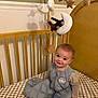 Grayson is registered to the contest to win money with this photo: baby, crib, mobile, knitted_toys, stars, moon, clouds, sleeping_bag, pacifier, wooden_furniture, nursery, child, smiling, indoor, cute, infant, checkered_bedding, warm_lighting, face, happy