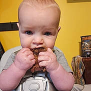 Rykir is registered to the contest to win money with this photo: baby, child, high_chair, food, eating, hands, face, blue_eyes, expression, yellow_wall, indoor, meal_time, messy, cute, infant, clothing, seat_belt, portrait, young_child, home