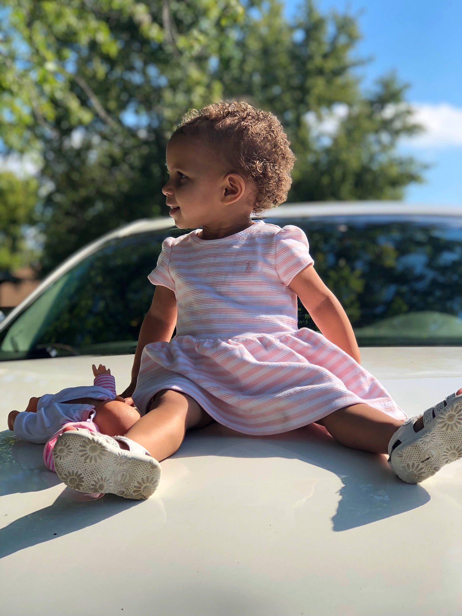Kayloni is registered to the contest to win money with this photo: automotive_exterior, baby, car, child, flash_photography, fun, grass, happy, human_leg, leisure, luxury_vehicle, person, play, recreation, sandal, sitting, sky, toddler, tree, vacation