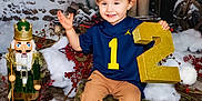Xanderlee is registered to the contest to win money with this photo: child, toddler, smiling, blue_jersey, baseball_cap, number_two, log_seat, nutcracker, winter_scene, snow, red_berries, candles, lantern, indoor, holiday_decor, brown_pants, black_shoes, festive, portrait, cute