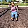 child, toddler, swing, playground, outdoor, park, tree, grass, blue_sky, sunny, jeans, plaid_shirt, smiling, happy, person, playing, daylight, casual_clothing, shoes, shadow