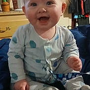 Declan is registered to the contest to win money with this photo: baby, infant, smile, pajamas, polka_dot, sitting, blanket, bedroom, indoor, cute, child, happy, face, hands, feet, furniture, plant, fan, clothing, home