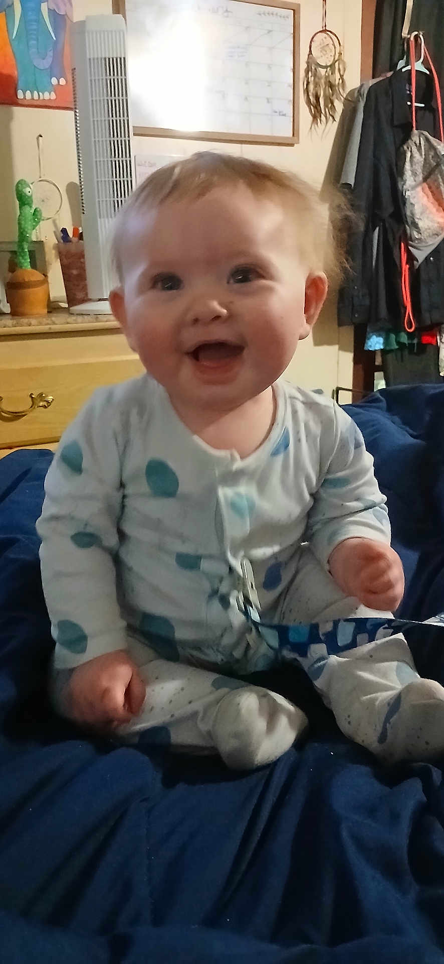 Declan is registered to the contest to win money with this photo: baby, infant, smile, pajamas, polka_dot, sitting, blanket, bedroom, indoor, cute, child, happy, face, hands, feet, furniture, plant, fan, clothing, home