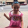 child, girl, princess_dress, pink_dress, disney_princess, candy, headband, outdoor, sidewalk, table, red_table, city, buildings, cars, smiling, person, young_child, curly_hair, playful, cute