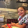 Isabella is registered to the contest to win money with this photo: child, smiling, portrait, restaurant, menu, table, hands, happy, wall, stone_wall, decor, sign, text, indoor, clothing, person, face, cute, dining, casual