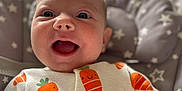 Daisy is registered to the contest to win money with this photo: baby, infant, smiling, happy, onesie, carrot_pattern, cushion, seat, face, mouth_open, eyes, hand, cute, child, indoor, soft_lighting, portrait, cozy, star_pattern, clothing