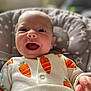 baby, carrot_pattern, child, clothing, cozy, cushion, cute, eyes, face, hand, happy, indoor, infant, mouth_open, onesie, portrait, seat, smiling, soft_lighting, star_pattern