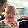 Adeline is registered to the contest to win money with this photo: baby, infant, adult_profile, car_interior, steering_wheel, window, car, seat, person, portrait, face, chubby_cheeks, pink_clothing, dashboard, rear_window, cloudy_sky, closeup, holding, expression, hair